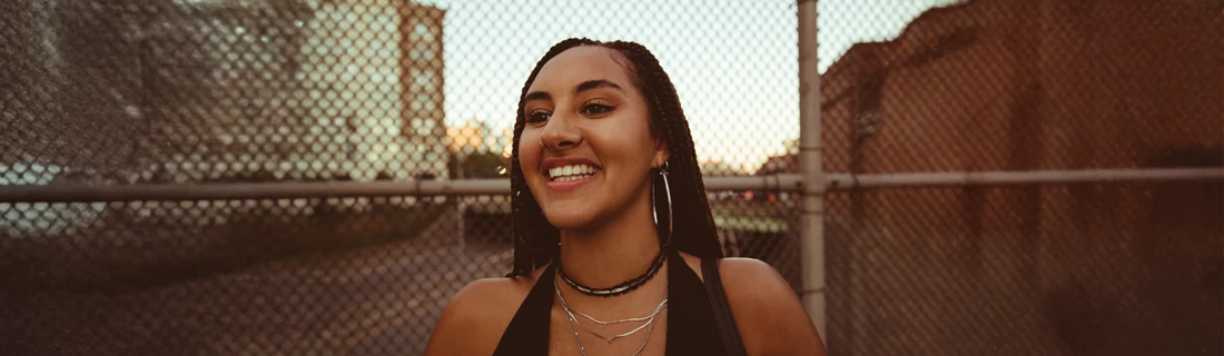 A woman smiling in front of a chain link fence.