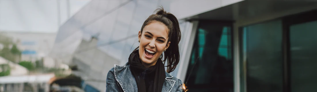 A woman with a ponytail, smiling in front of an office building.