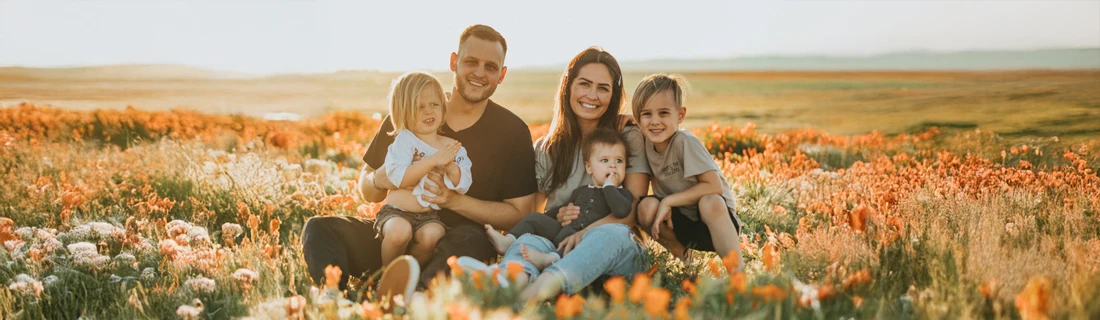 A family of 5 smiling in a field of flowers.